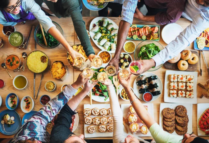 Group of people enjoying a diverse spread of food, raising their glasses in a toast, showcasing a communal dining experience