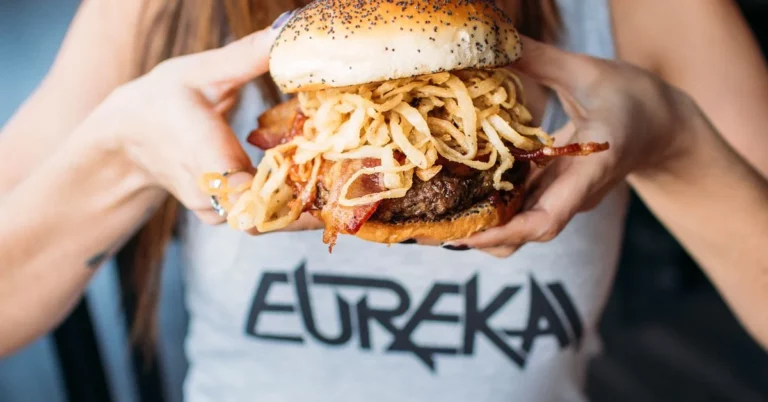 Eureka Cowboy Burger with crispy onions, bacon, and a beef patty held by a person wearing a Eureka t-shirt